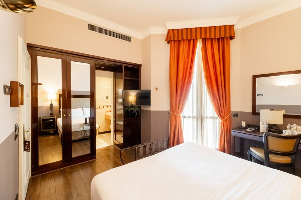 Habitación de hotel con cama, escritorio, silla y un espejo grande.