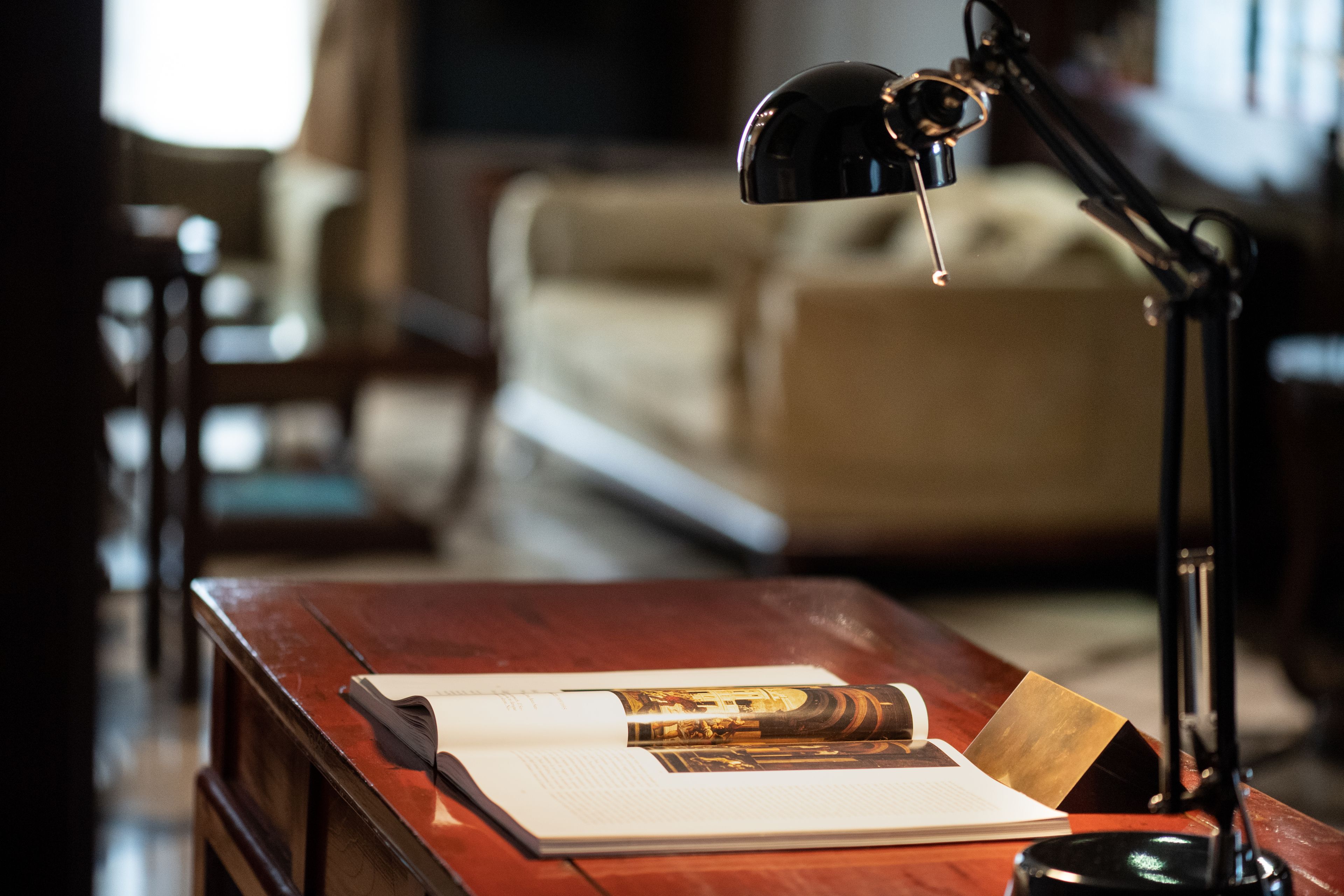 A wooden desk with a book, a rolled-up magazine, and a lamp.