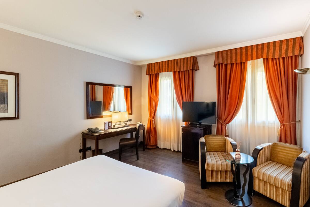 Una habitación de hotel con cama, escritorio, televisor y dos sillones.