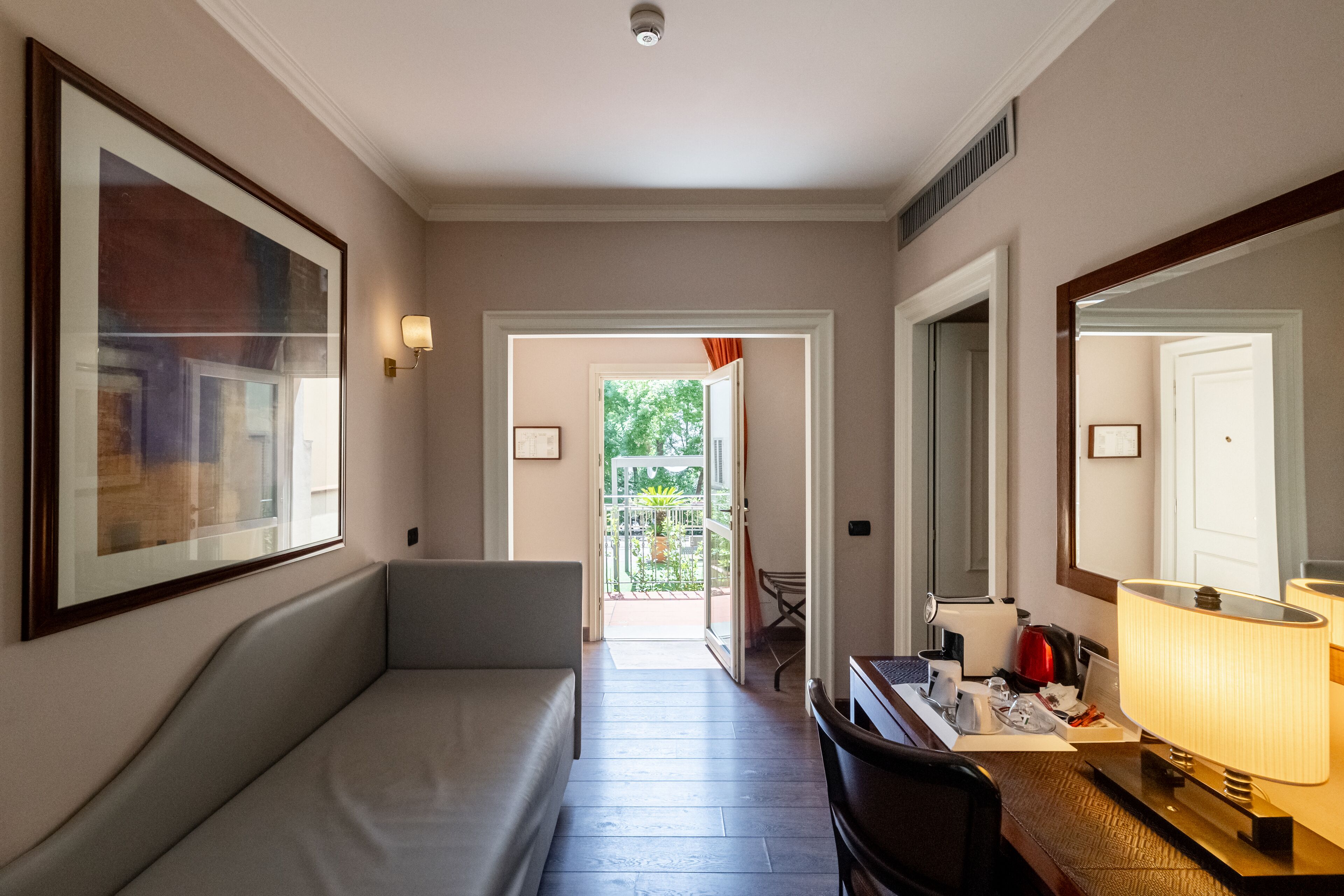 Een hotelgang met een bank, een bureau met een lamp en een grote spiegel.