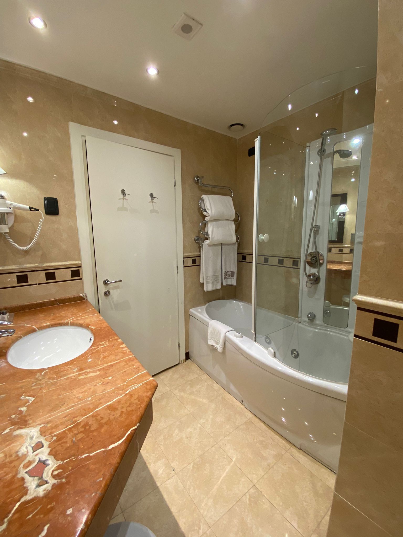 A bathroom with a marble sink, a bathtub, a glass-enclosed shower, and a white door.