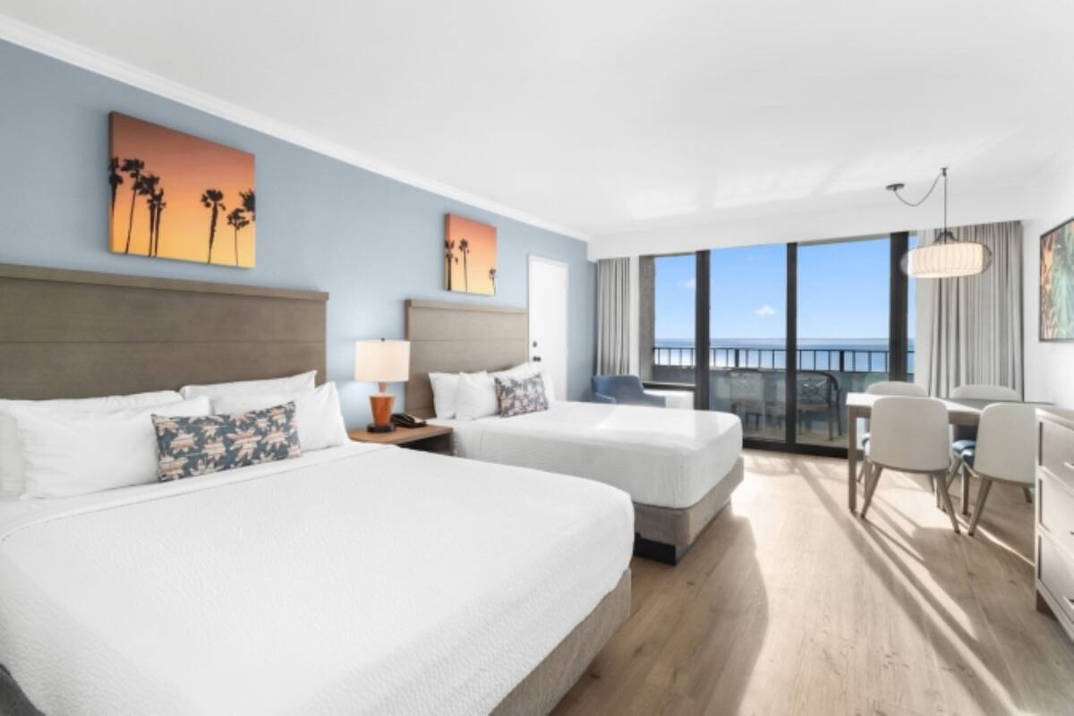 A hotel room with two beds, a desk, and a view of the ocean.