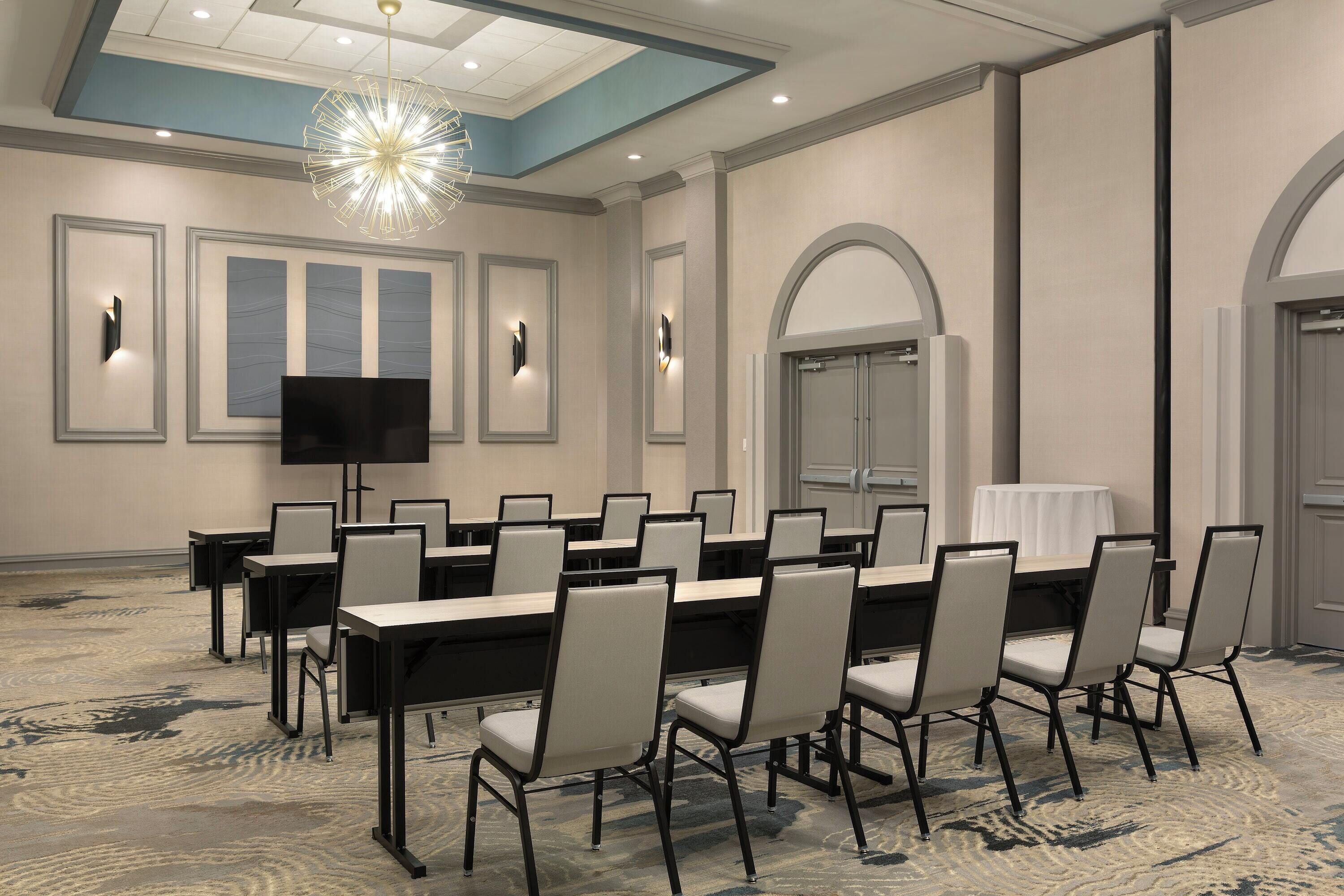 A conference room with a long table, chairs, a flat-screen TV, and a ceiling light fixture.