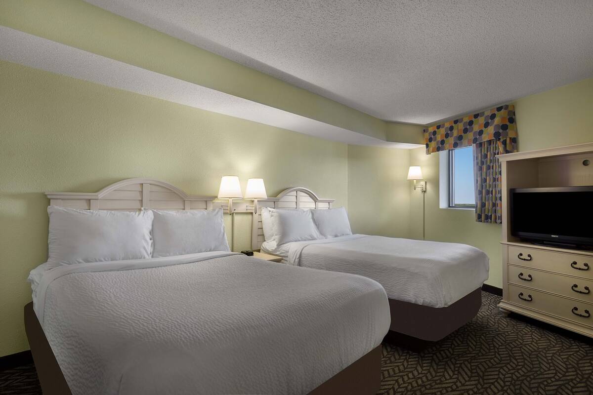 A hotel room with two beds, a television, and a window with curtains.