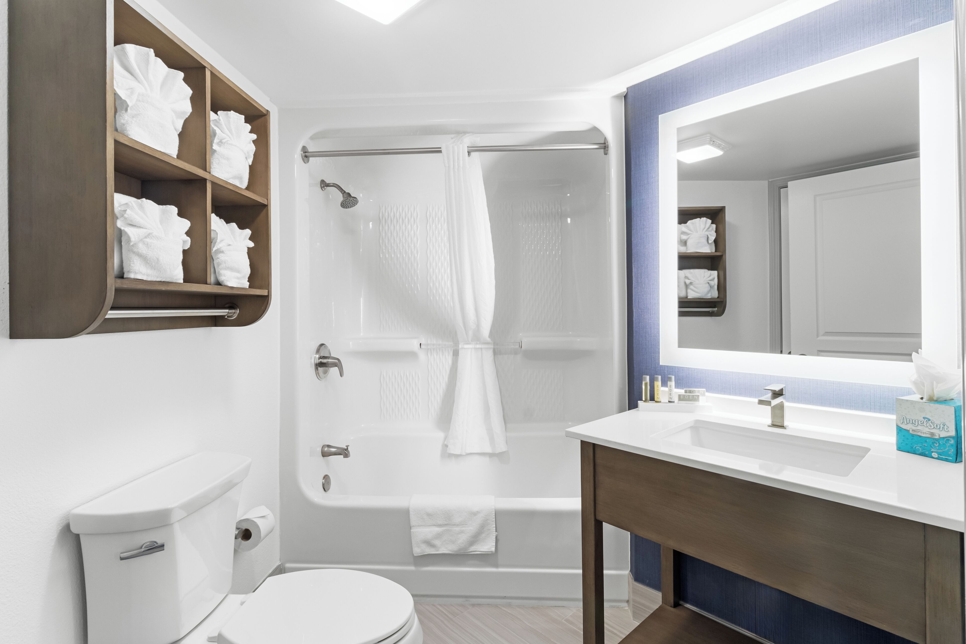 A bathroom with a toilet, a bathtub with a shower curtain, a sink with a mirror, and shelves with towels.