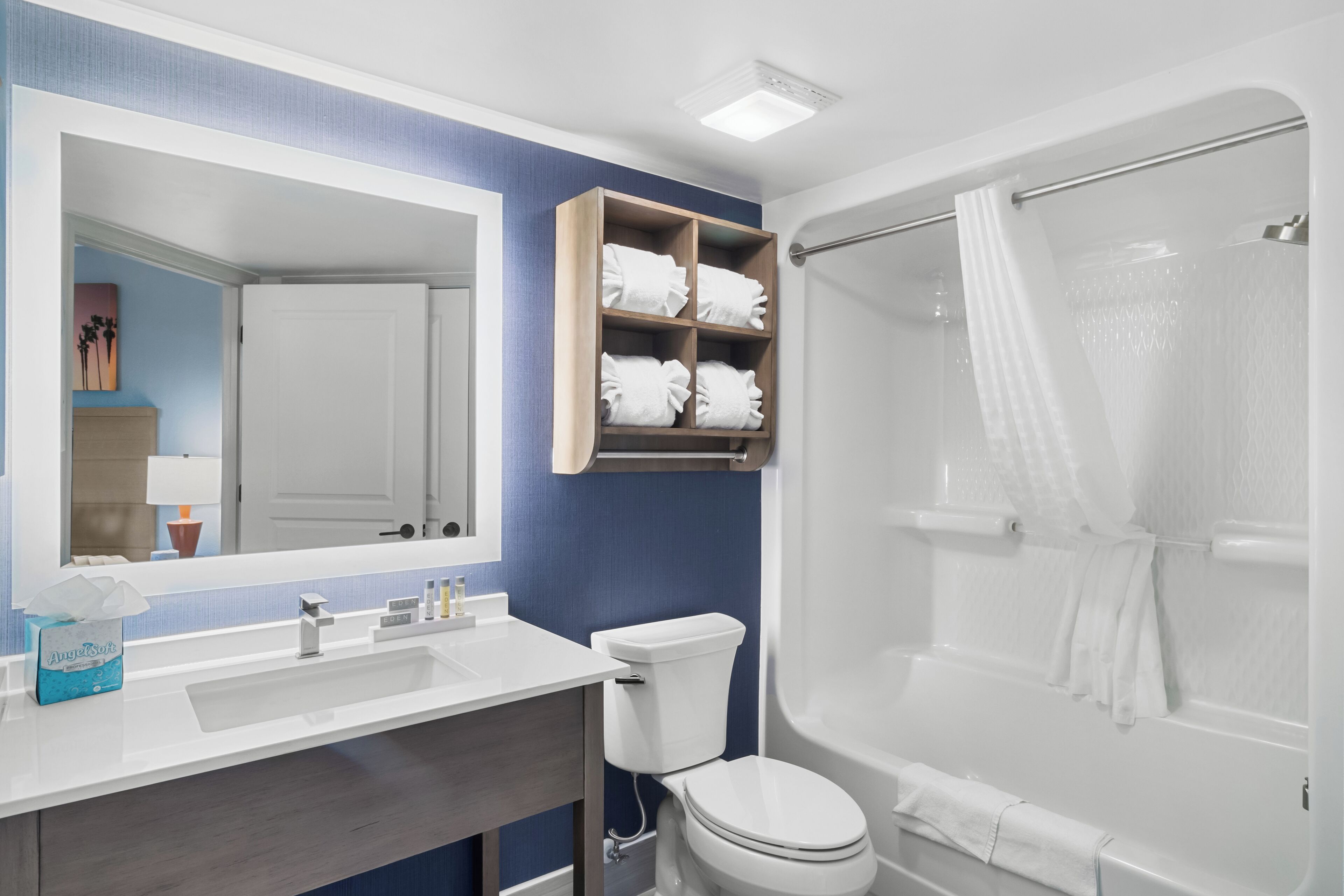 A bathroom with a white sink, mirror, and toilet. There is a shower with a glass door and a towel rack above the toilet.