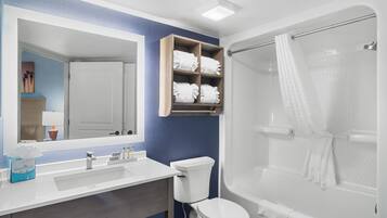 A bathroom with a white sink, mirror, and toilet. There is a shower with a glass door and a towel rack above the toilet.