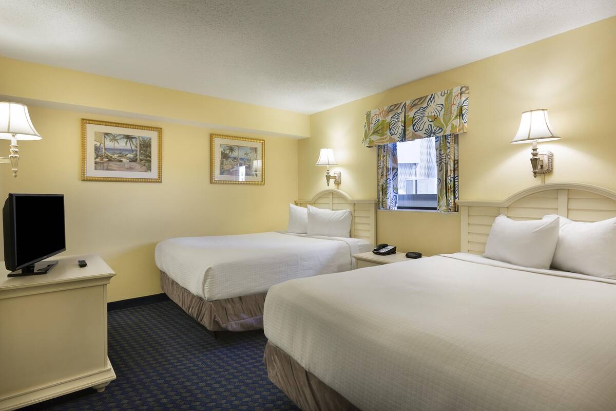 A hotel room with two beds, a television, and two wall-mounted lamps.