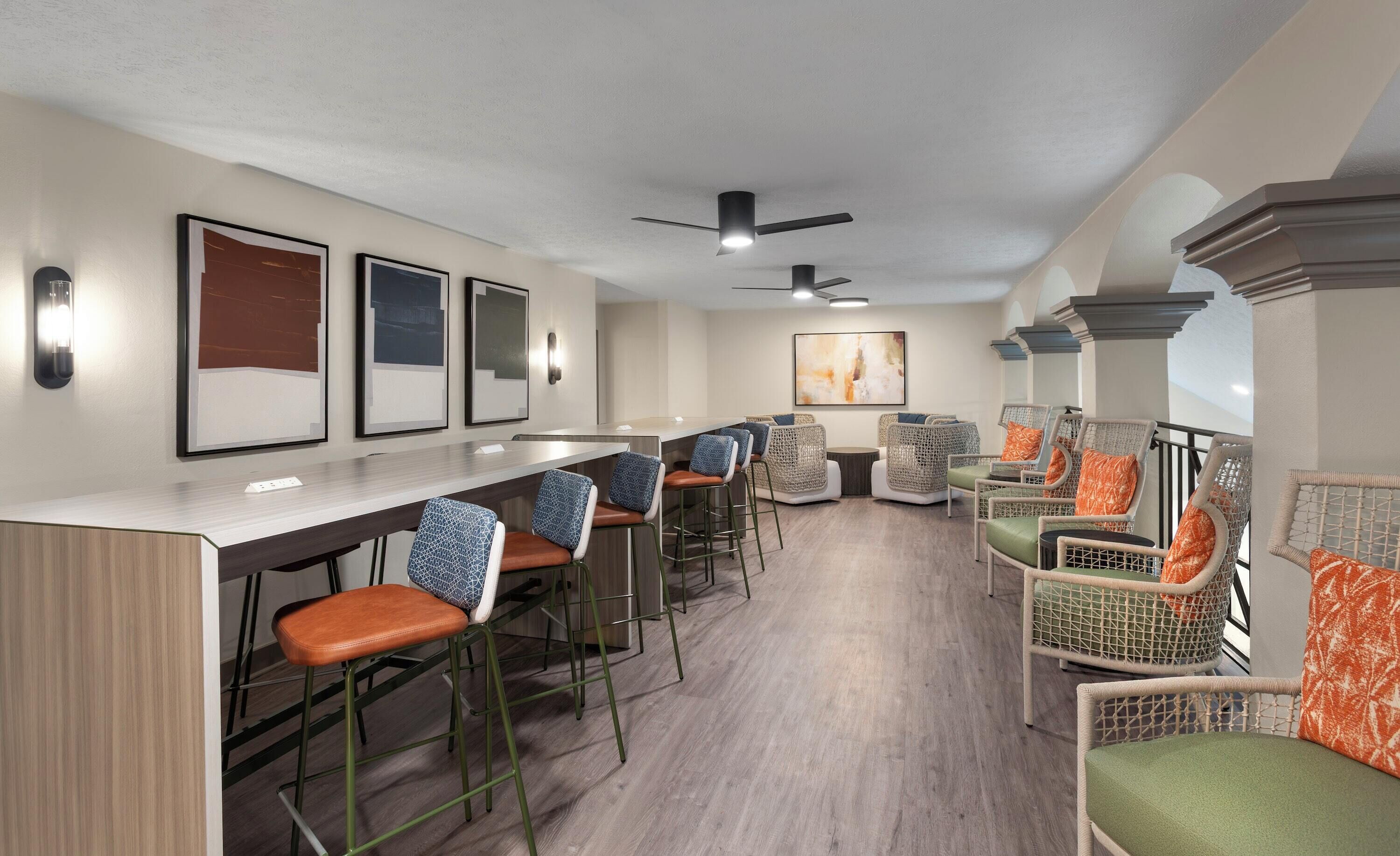 A bar area with high stools, wicker chairs, and a ceiling fan.