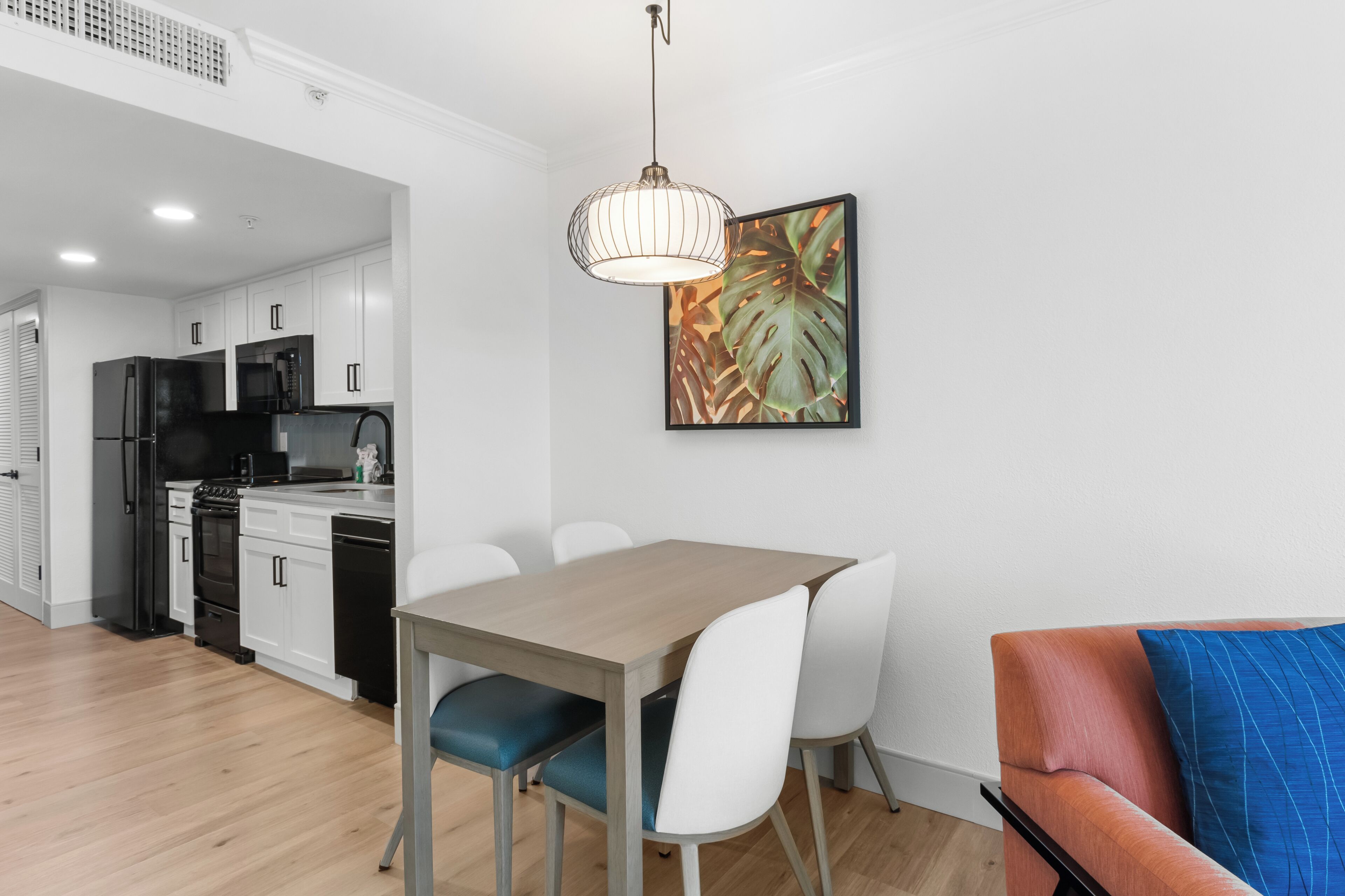 A modern kitchen with white cabinets, a dining table with chairs, and a hanging pendant light.