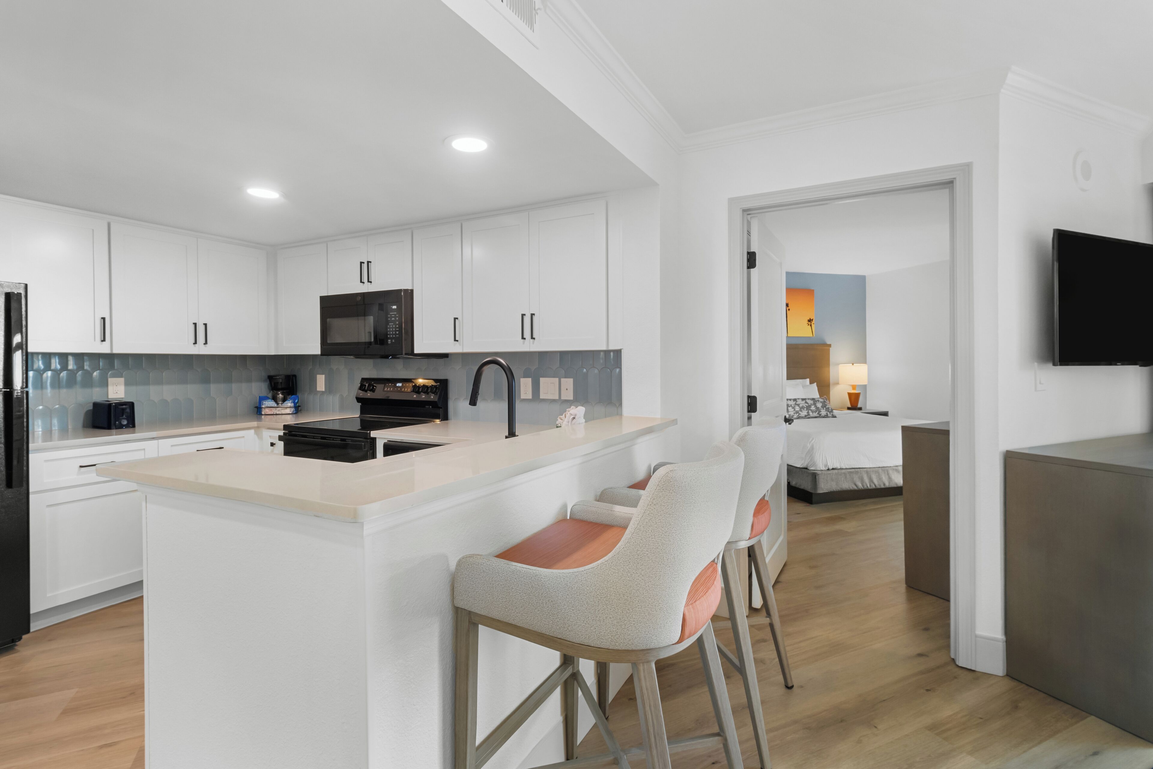 Une cuisine moderne avec des meubles blancs, un îlot central doté de tabourets, un four à micro-ondes et une cuisinière.