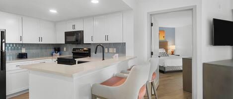 A modern kitchen with white cabinets, a central island with bar stools, a microwave, and a stove.