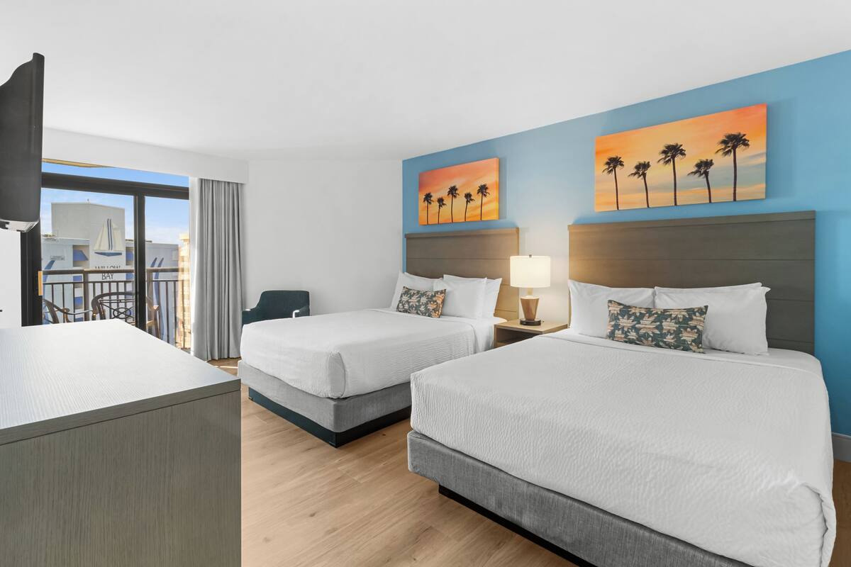 Quarto de hotel com duas camas, uma escrivaninha e vista para a cidade.