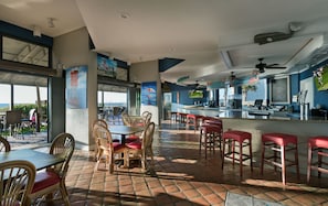 A restaurant with outdoor seating, a bar area, and a view of the ocean.