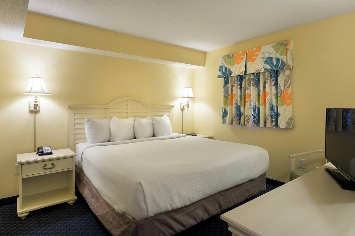 Quarto de hotel com cama, abajures, televisão de tela plana e cortina florida.