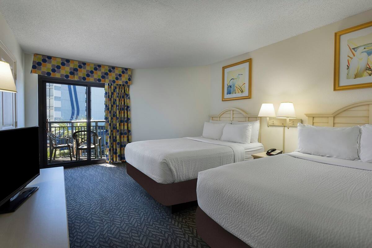 Quarto de hotel com duas camas, uma escrivaninha, uma televisão e varanda com vista.