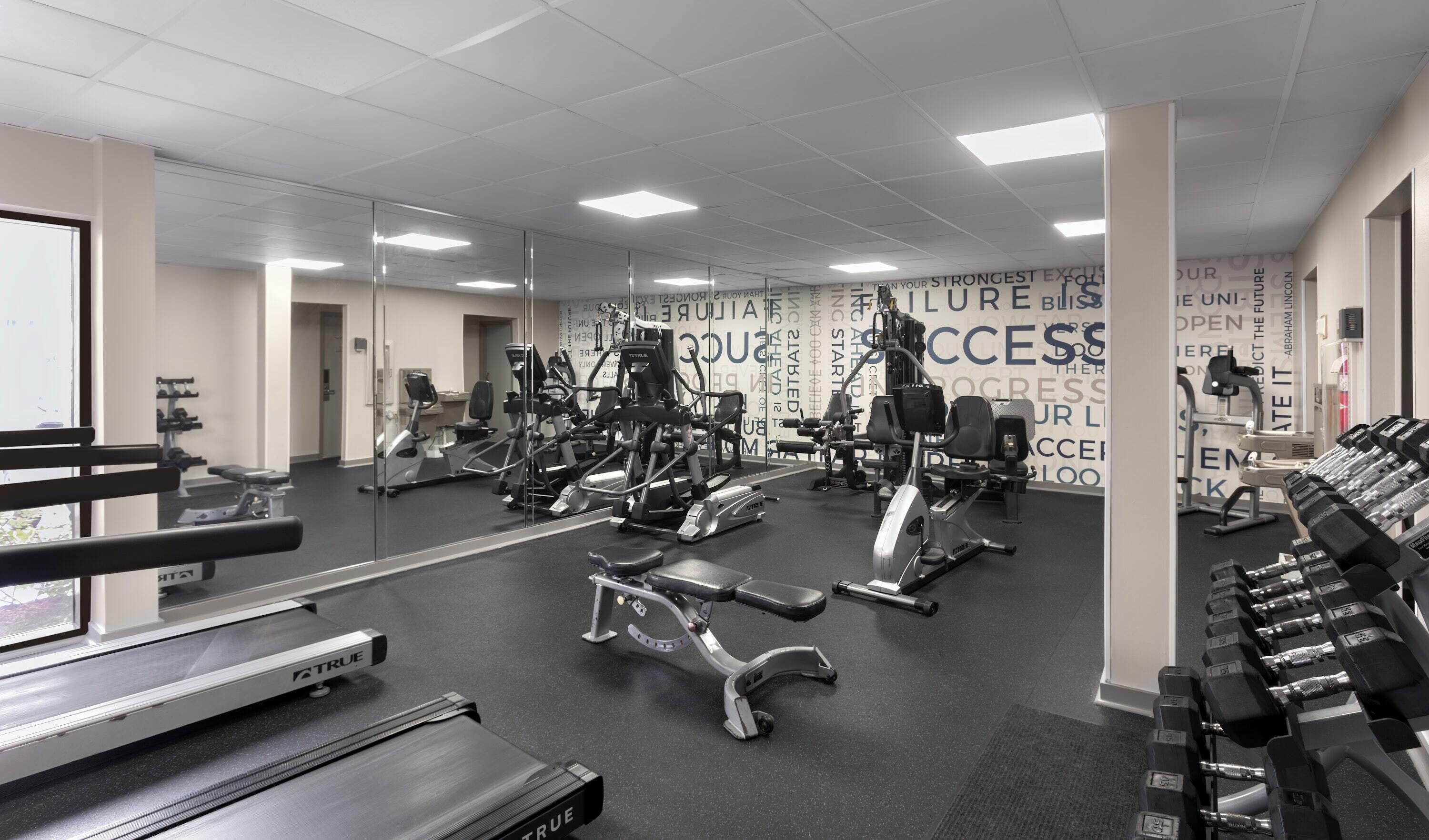 A gym with various exercise equipment, a mirrored wall, and motivational text.