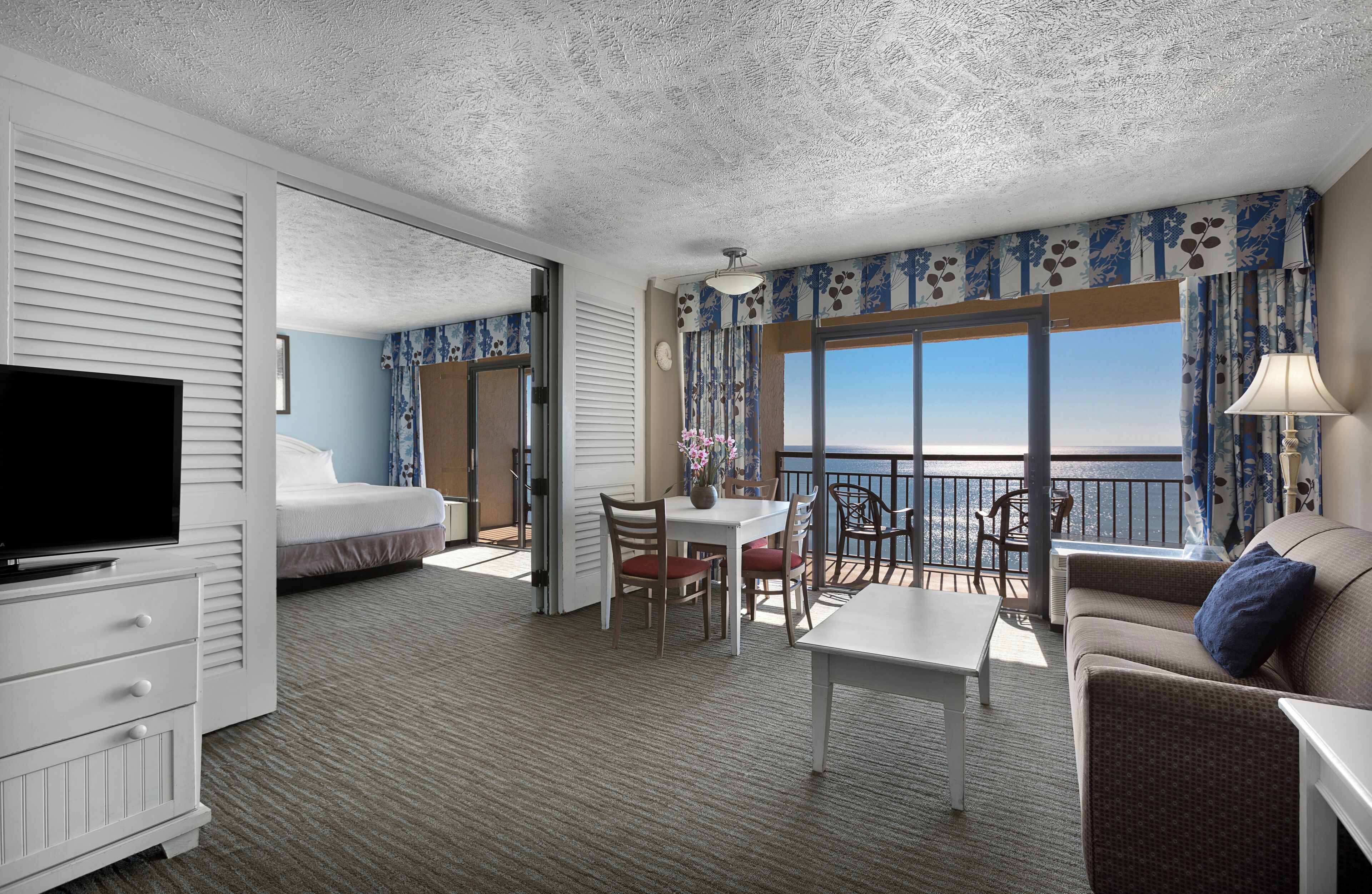 Une chambre d’hôtel avec un balcon, un lit, une télévision, un coin repas et un canapé.