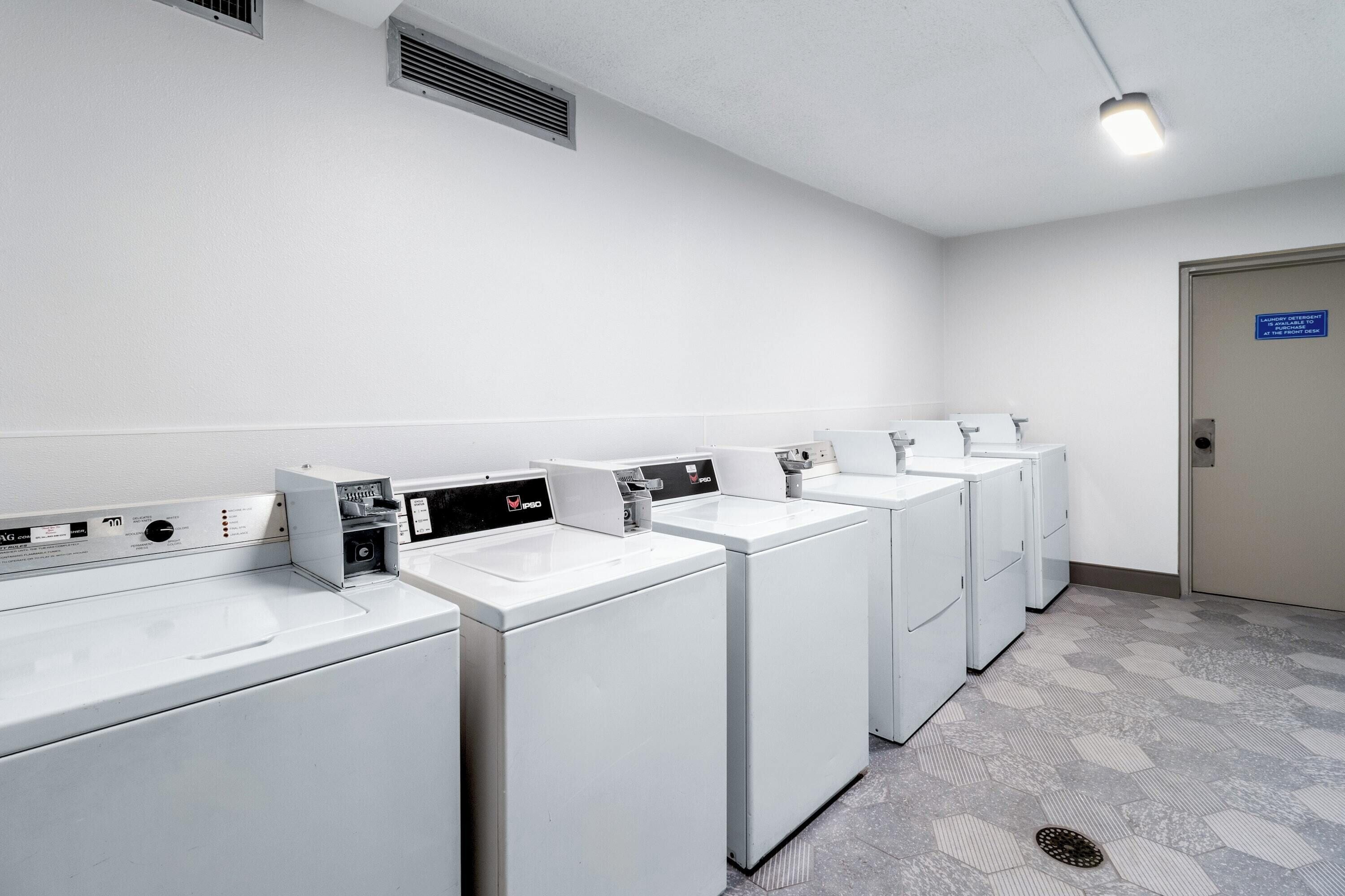 A row of white front-loading washers and dryers in a clean, well-lit laundry room with a hexagonal patterned floor.