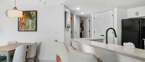 Una cocina moderna con armarios blancos, un refrigerador negro y una zona de comedor con una mesa y sillas de madera.
