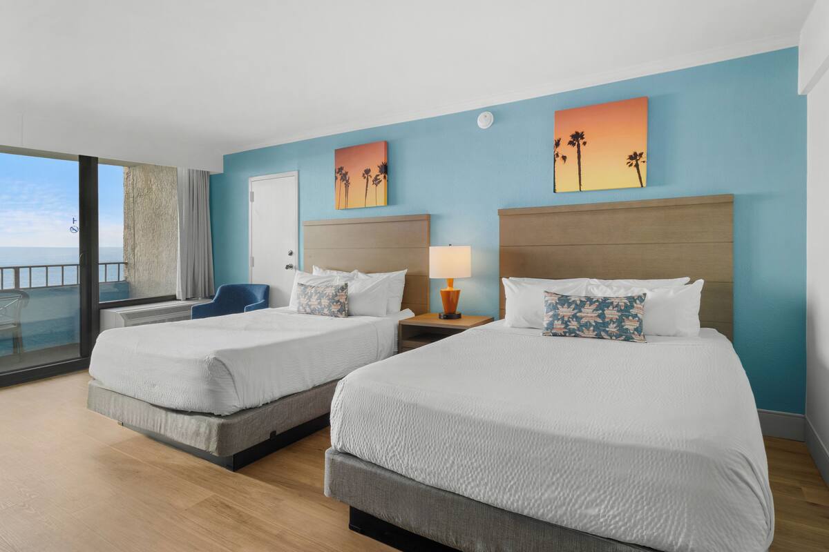Quarto de hotel com duas camas, uma varanda e vista para o mar.