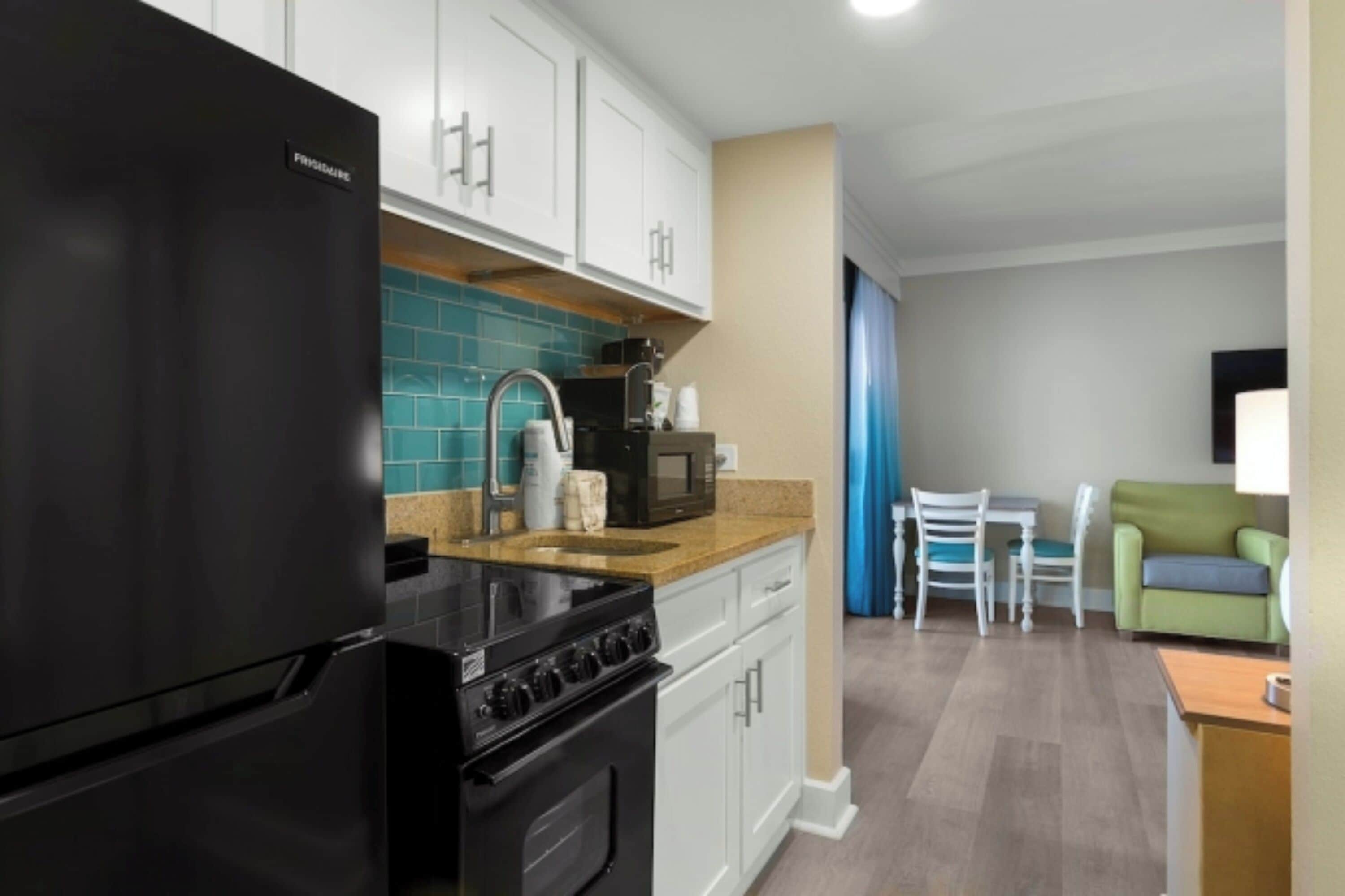 A modern kitchen with a black refrigerator, a stove, and a microwave. There is a dining area with a table and chairs.