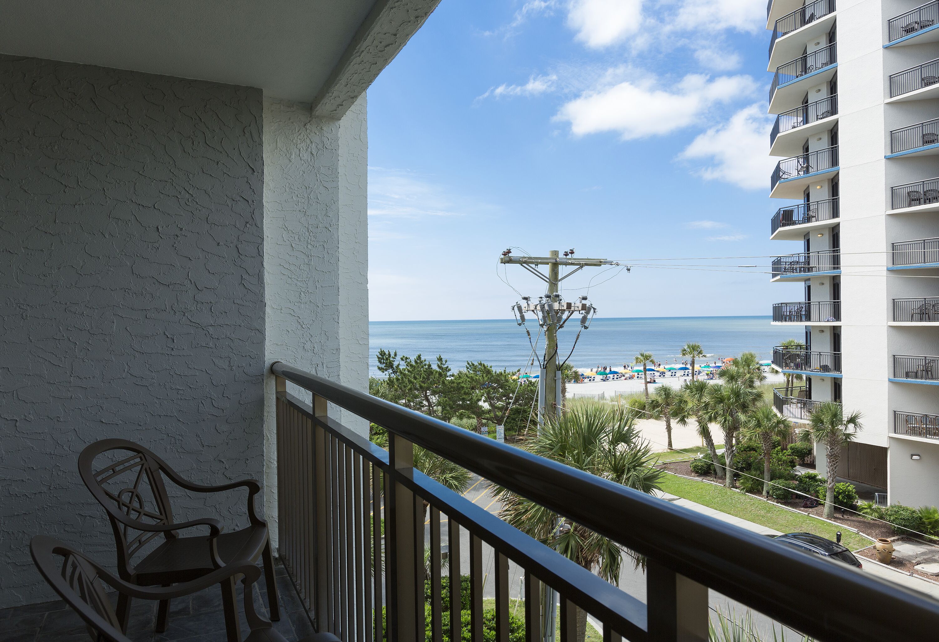 A balcony with a view of the beach and a building with multiple balconies.