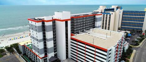 Um hotel com vários andares, piscina no terraço e vista para a praia e oceano.