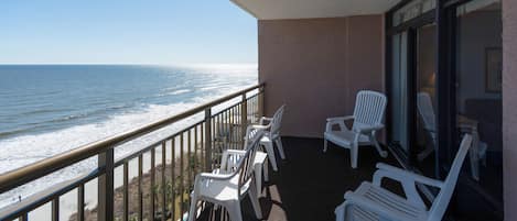 A balcony with a view of the ocean, equipped with white plastic chairs and a table.