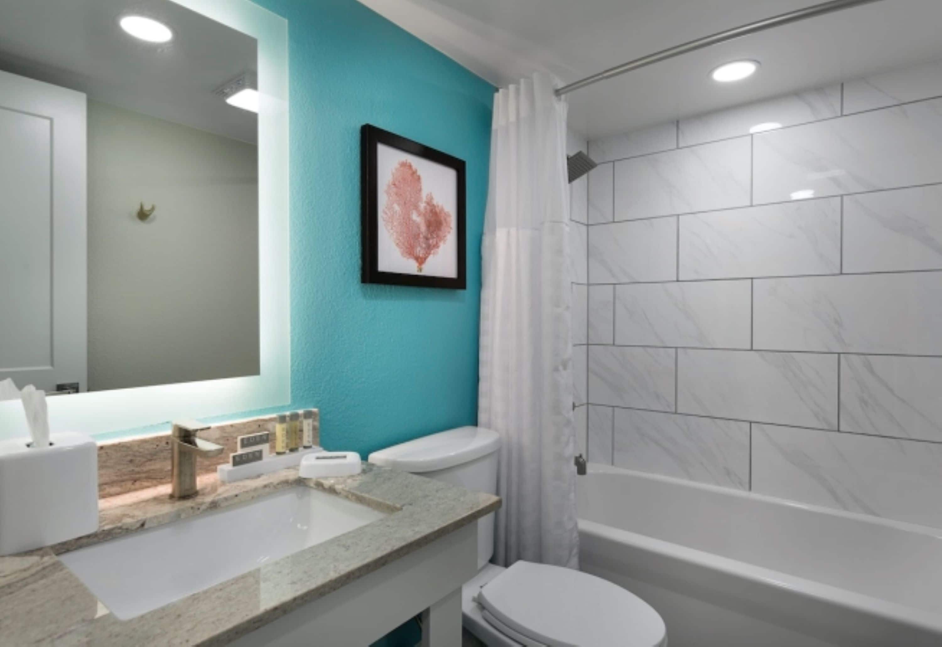 Un baño moderno con una pared de acento color turquesa, un lavamanos blanco, un inodoro y una zona de ducha.