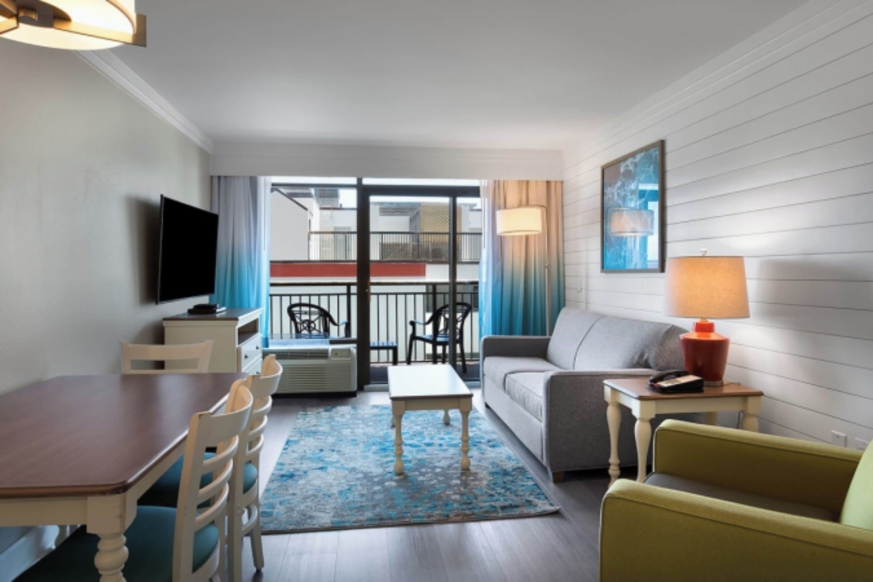 A modern living room with a dining area, a sofa, a TV, and a balcony with a railing.