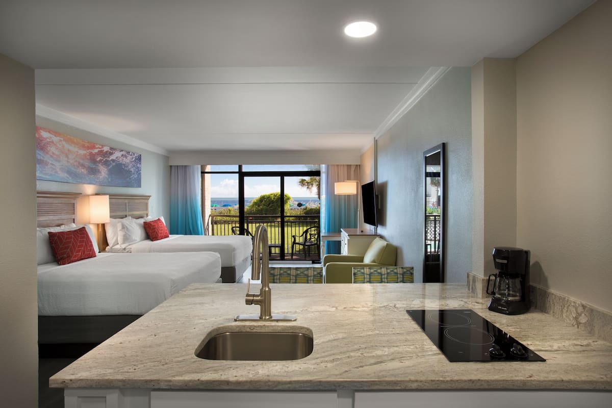 A hotel room with a kitchen area, two beds, a TV, and a balcony with a view.