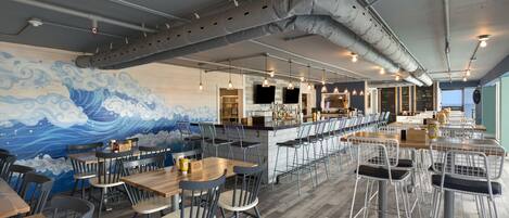 A restaurant with a wave mural, bar area, and multiple seating arrangements.