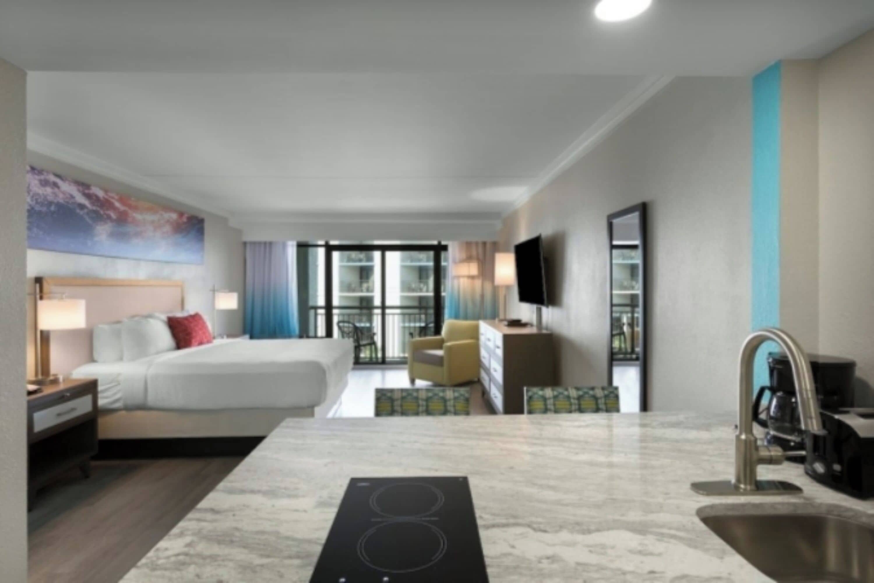 Ein modernes Hotelzimmer mit Bett, Schreibtisch, integriertem Herd, Spüle und Fernseher.