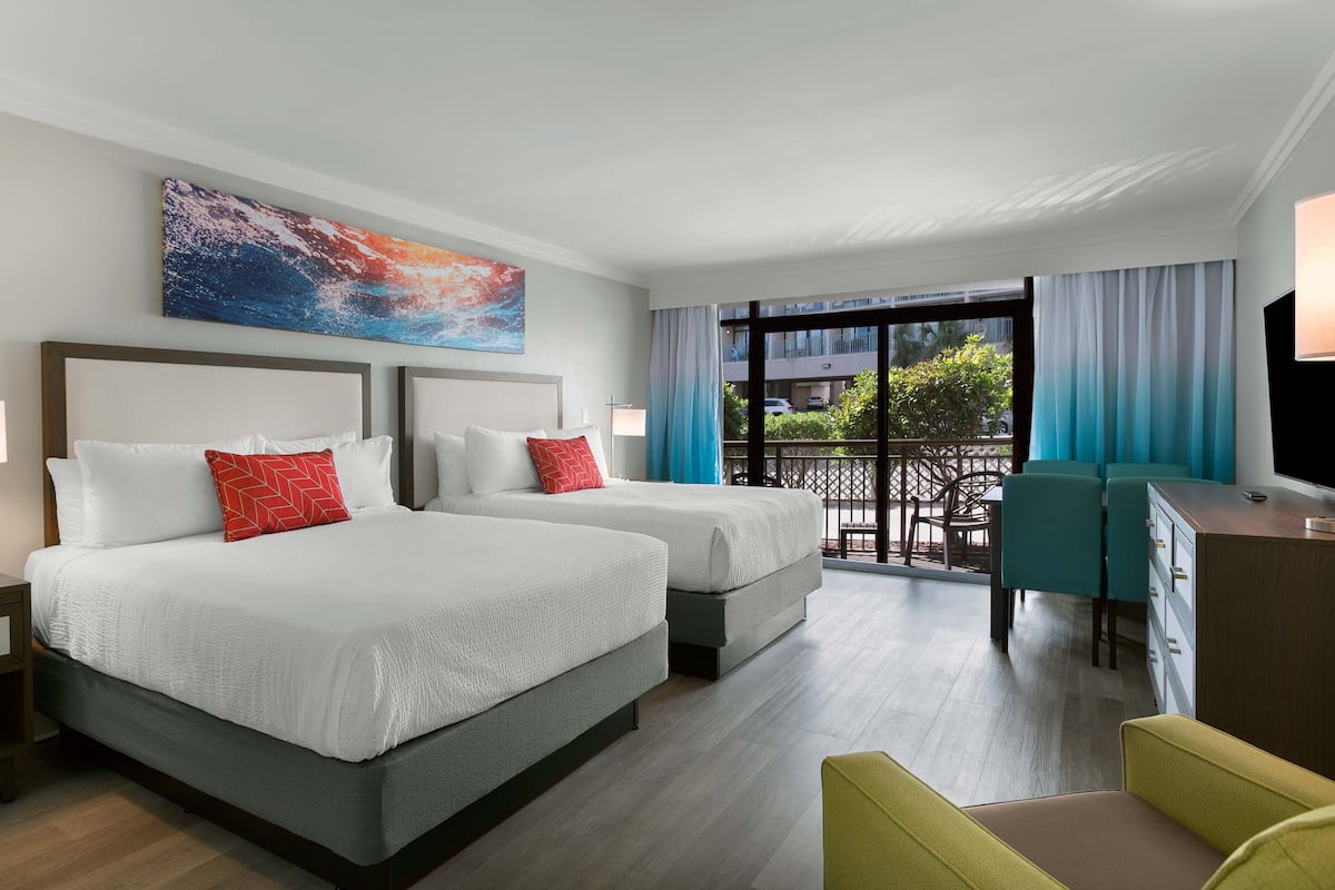 A hotel room with two beds, a balcony with a view, a desk with a chair, and a TV.