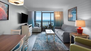 Una habitación de hotel moderna con balcón, zona de comedor, sofá y televisor.
