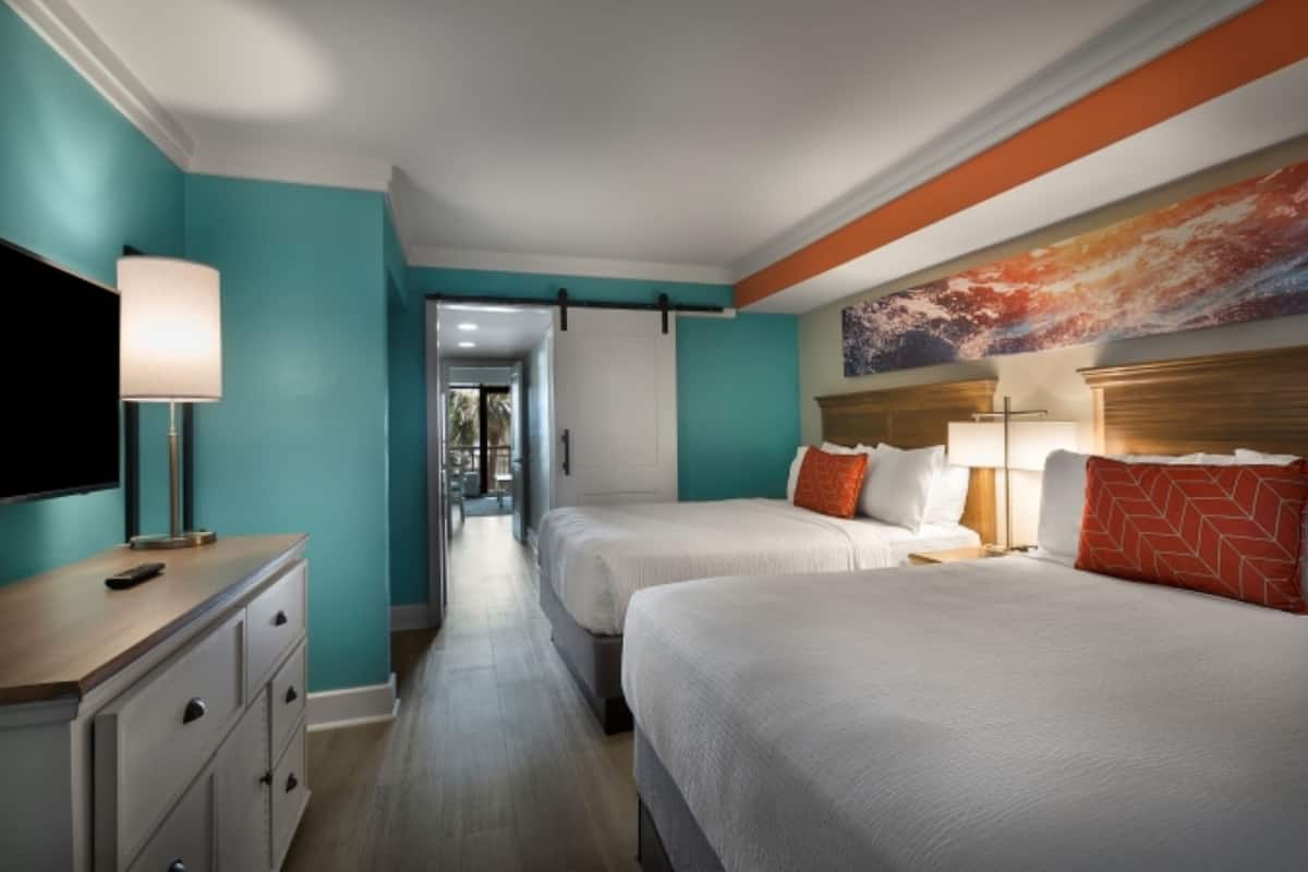 A hotel room with two beds, a TV, a desk, and a painting on the wall.