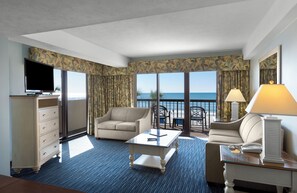 A hotel room with a sofa, armchair, coffee table, TV, and a view of the ocean. - Grande Cayman Resort (Myrtle Beach)