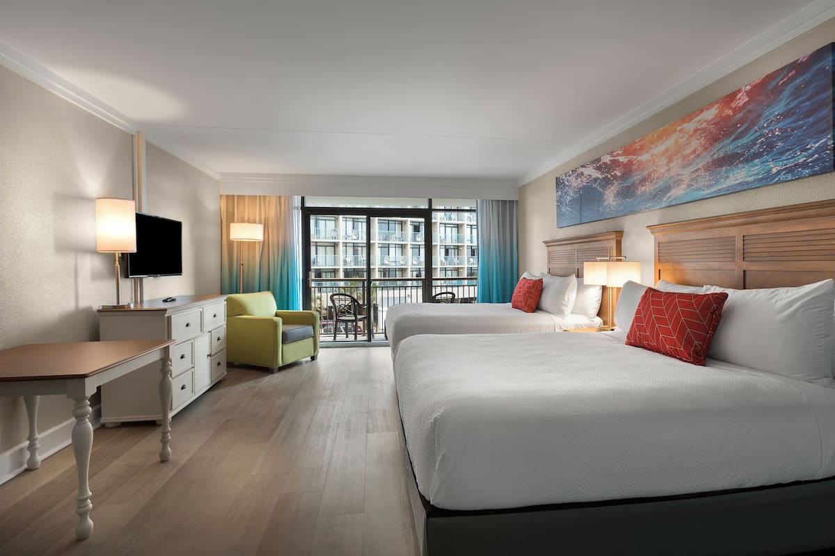 A hotel room with two beds, a desk, a chair, a TV, and a balcony with a view of the building.