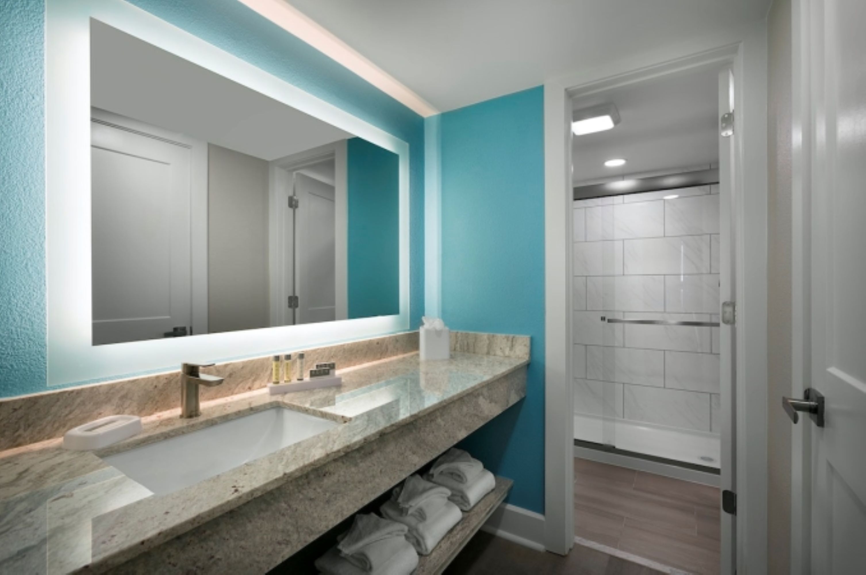 A bathroom with a large mirror, a marble countertop, and a shower area.