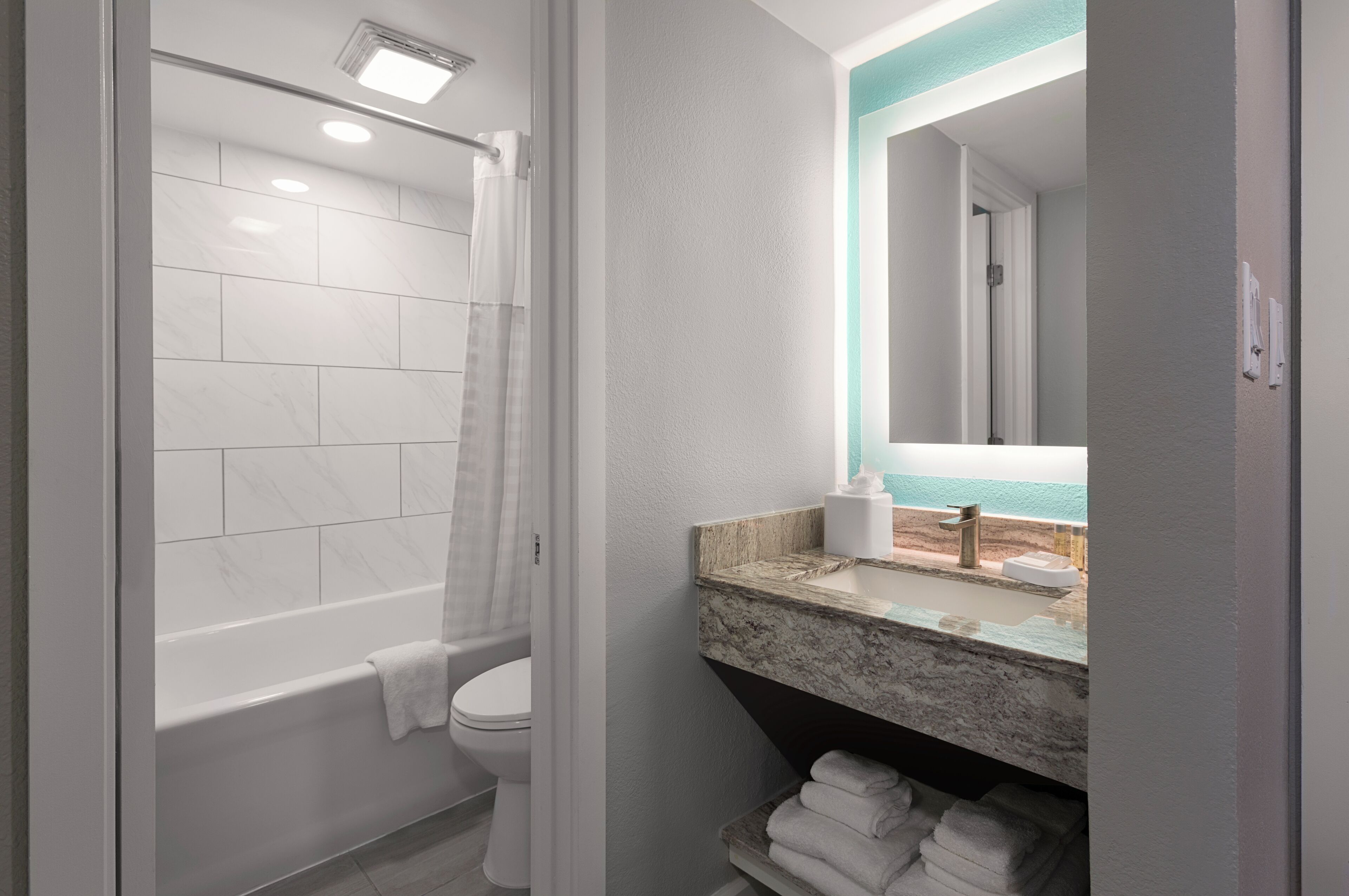 Une salle de bain moderne équipée d’une baignoire, de toilettes et d’un meuble-lavabo avec un plan de travail en marbre et un grand miroir.