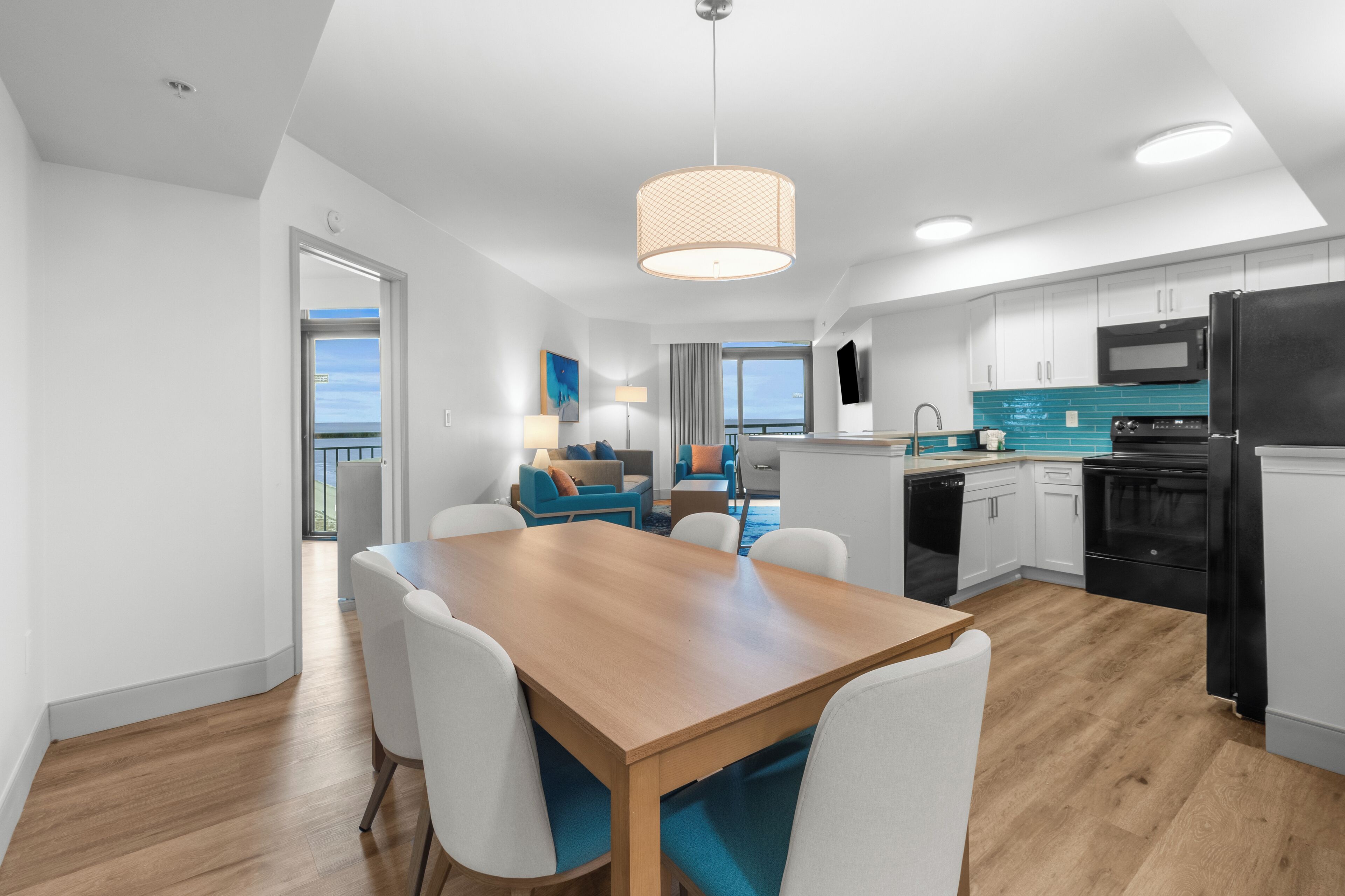 A modern kitchen with white cabinets, a black refrigerator, and a wooden dining table with white chairs.