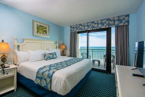 A hotel room with a bed, a desk, a chair, a TV, and a balcony with a view of the ocean. - Caribbean Resort & Villas (Myrtle Beach)