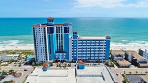 A large hotel with multiple floors and a prominent tower, located near a beach with the ocean in the background. - Caribbean Resort & Villas (Myrtle Beach)