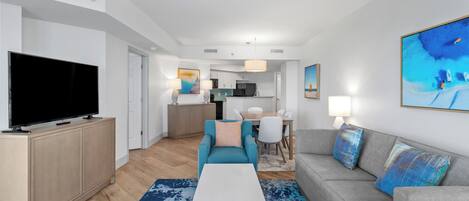 A modern living room with a flat-screen TV, a sofa, a coffee table, and a kitchen in the background.