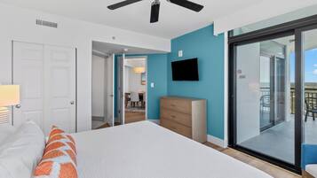 Une chambre à coucher comprenant un lit, une commode, un téléviseur et une porte-fenêtre coulissante donnant sur un balcon.