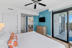 Une chambre à coucher comprenant un lit, une commode, un téléviseur et une porte-fenêtre coulissante donnant sur un balcon.