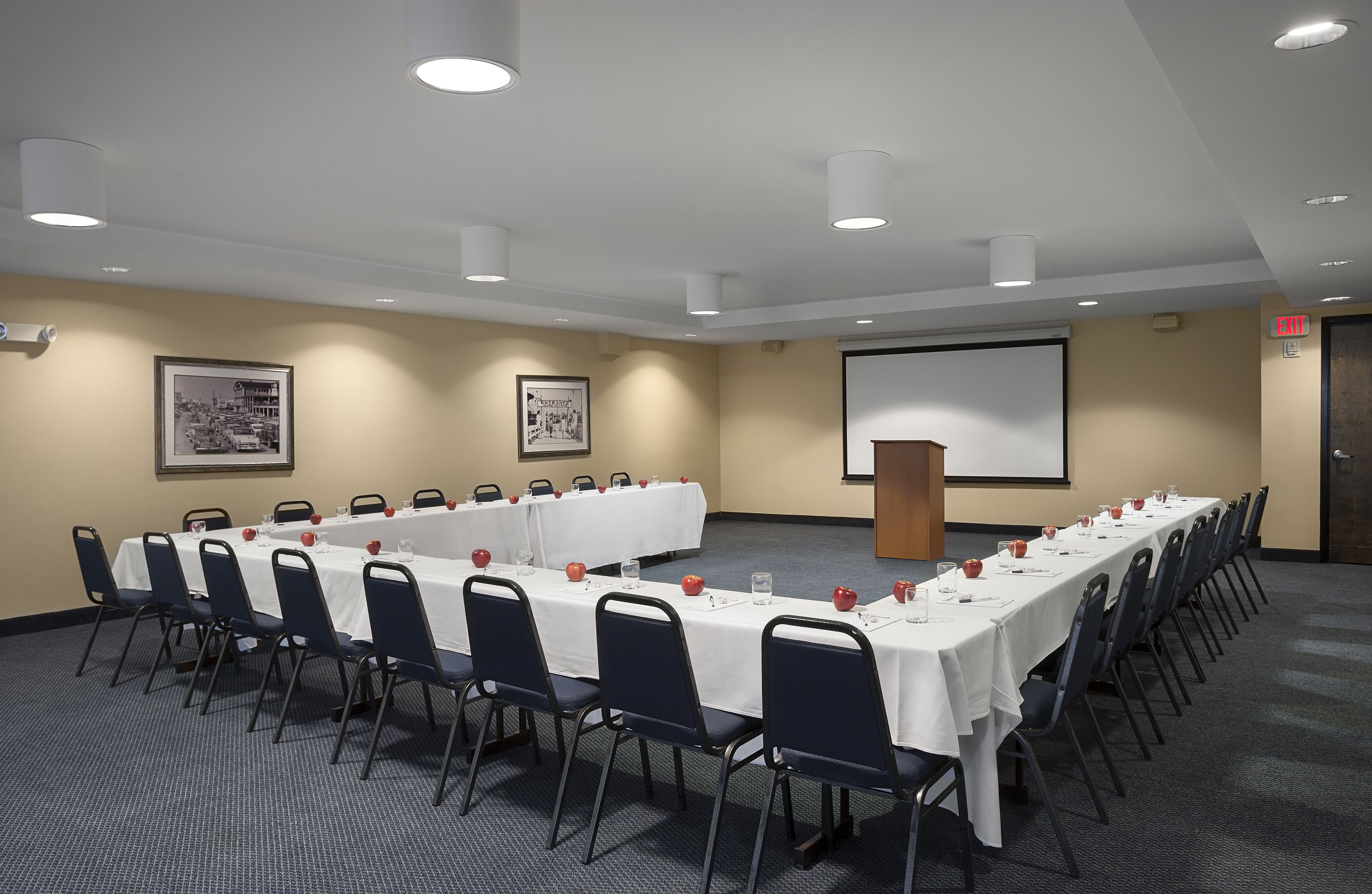 A conference room with a long table, chairs, a projector screen, and a podium.