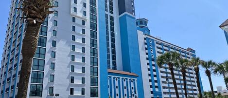 A multi-story hotel with a registration area, palm trees, and a clear blue sky.