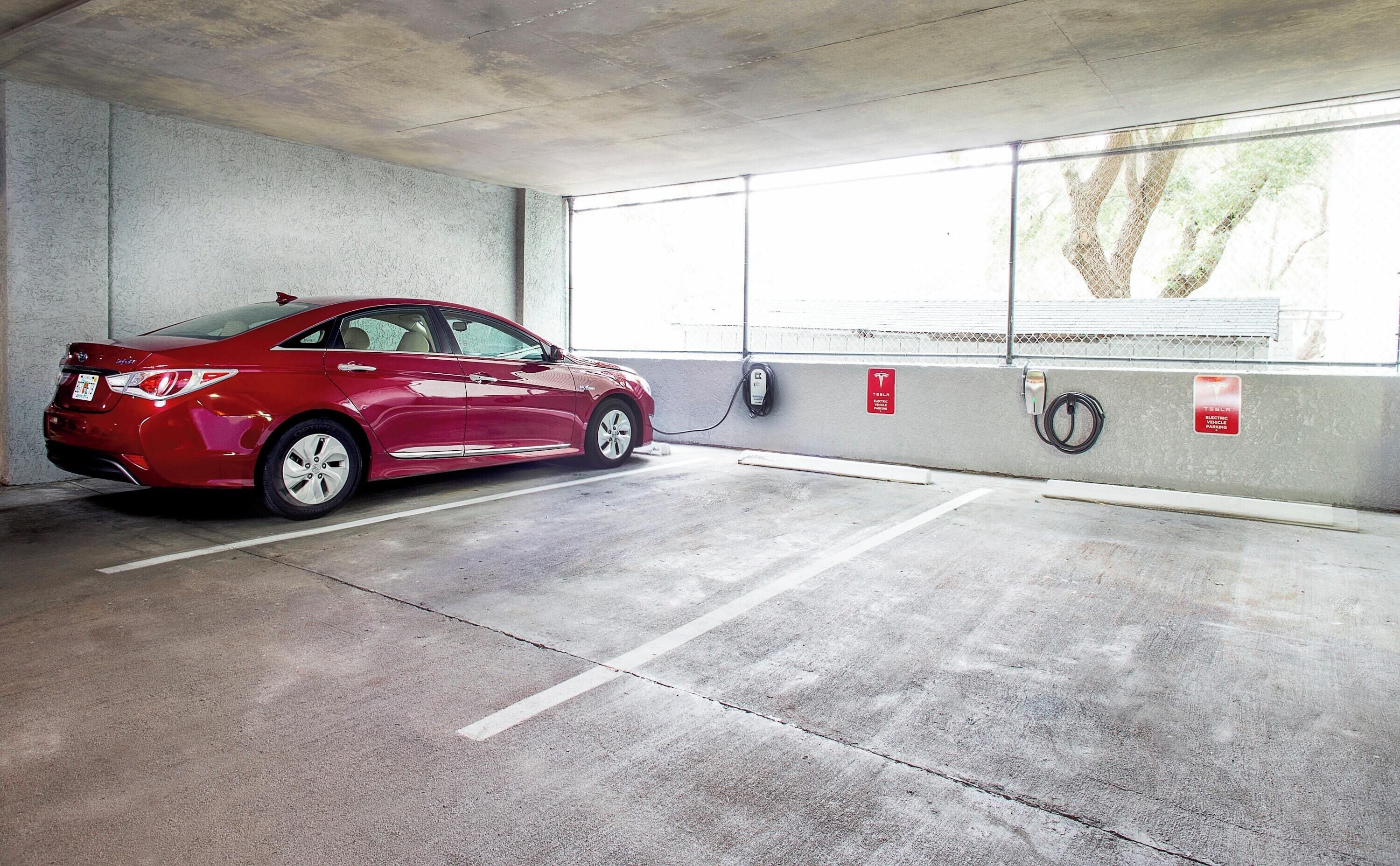 Punainen auto on pysäköity sähköautojen latausasemalle, jossa on betonilattia ja ikkunallinen seinä.